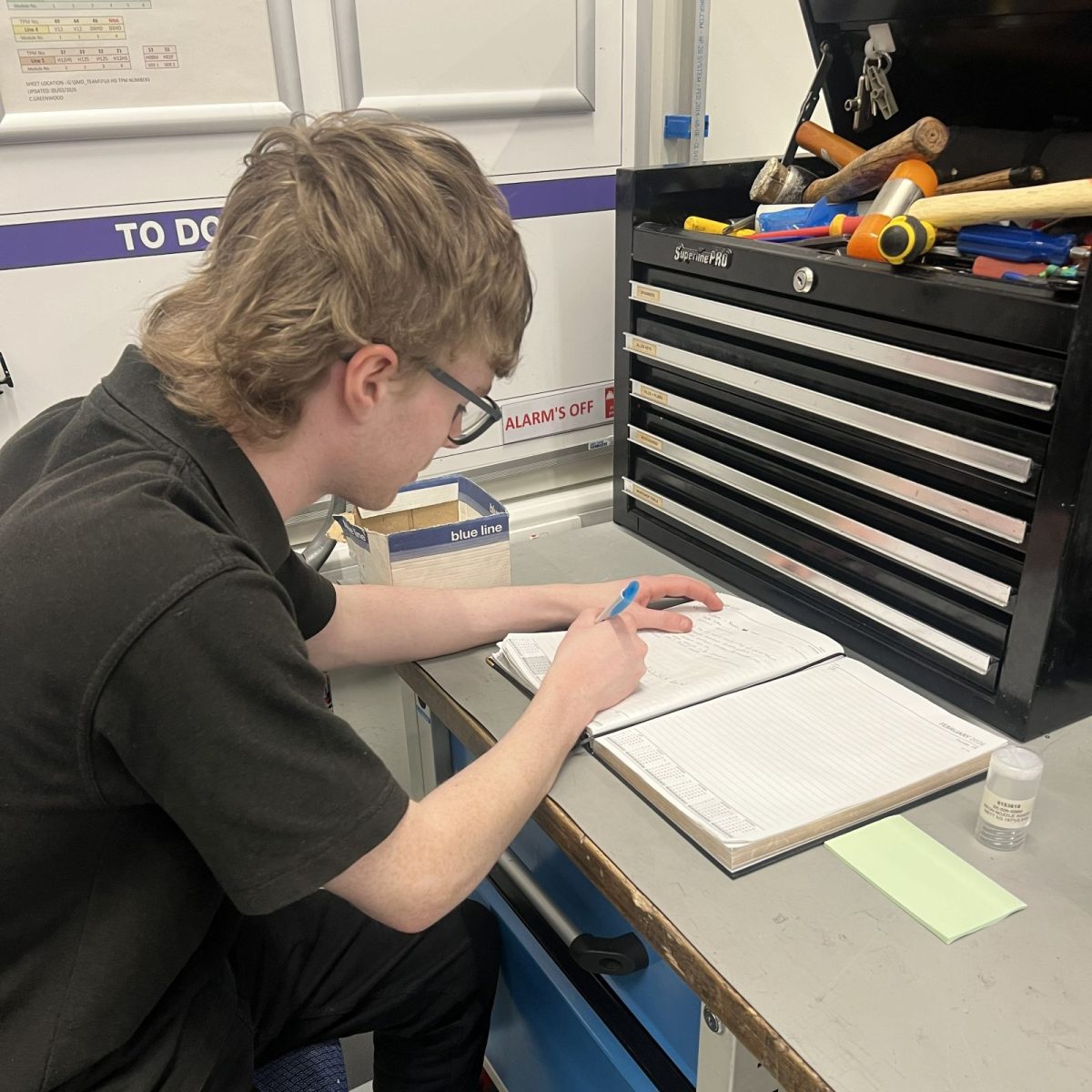 Maintenance and Operations Engineering Technician Troy, writing in a notebook on a worktable.