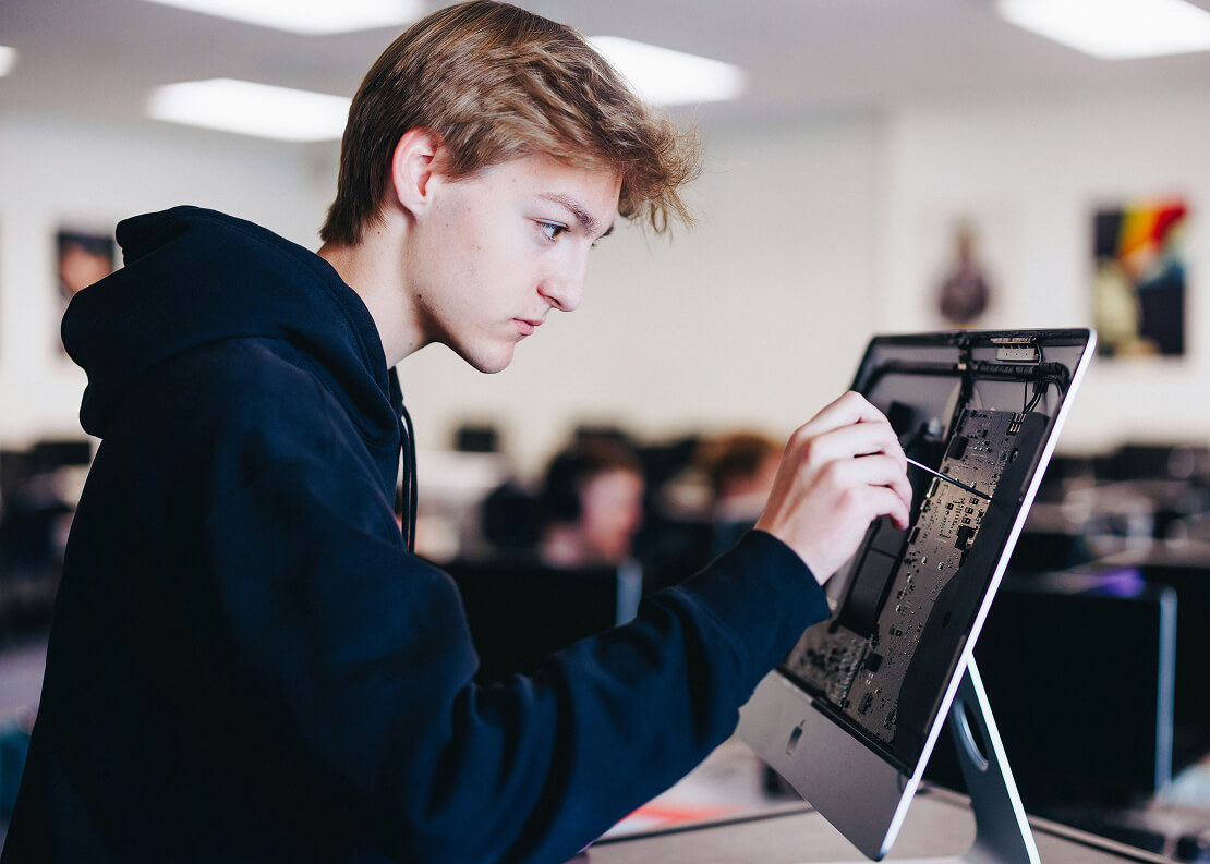 A young man working on the back of a computer monitor attempting to fix it