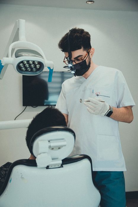 A male dental nurse with a patient. He is wearing a touch, glasses and face mask