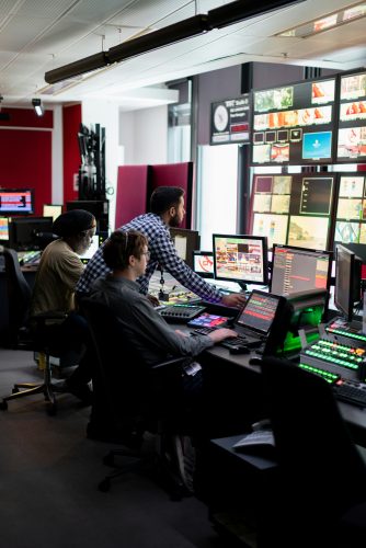 Broadcasting technicians in a broadcast room in front of lots of screens showing what's going on on the other side of the cameras