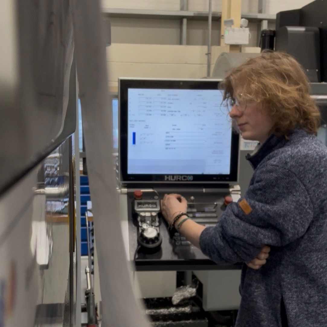 Maintenance and Operations Engineering Technician Ben, stood at the control panel screen of a large industrial CNC machine.