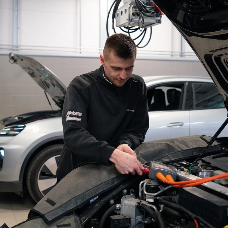 Electric Vehicle Technician Callum, working under the hood of a car, in the garage.