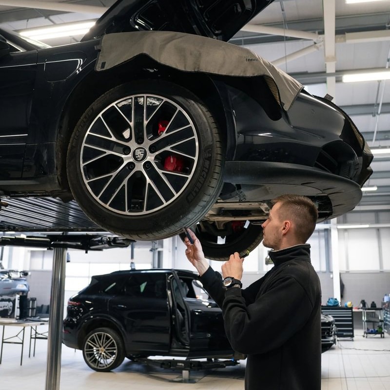 Electric Vehicle Technician Callum, in the garage, working on the underside of a car, hoisted up on a lift.