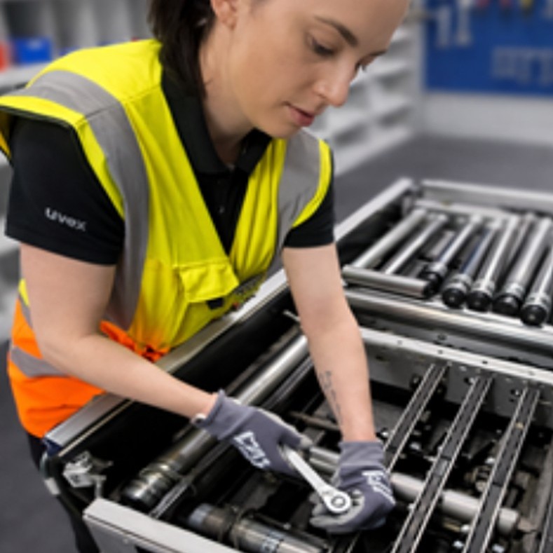 Mechatronics Technician Chloe, wearing a hi-vis vest and gloves, using a wrench to tighten equipment.