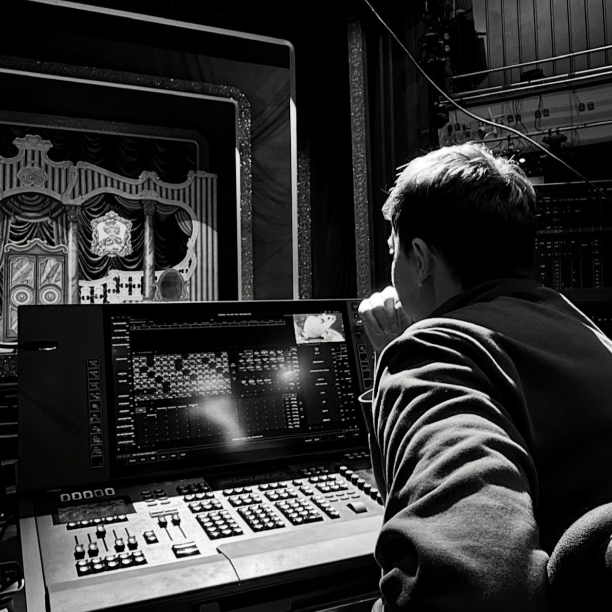 Creative Venue Technician Declan, sat at a lighting mixing desk at the back of a theatre, following along and cueing the lights.