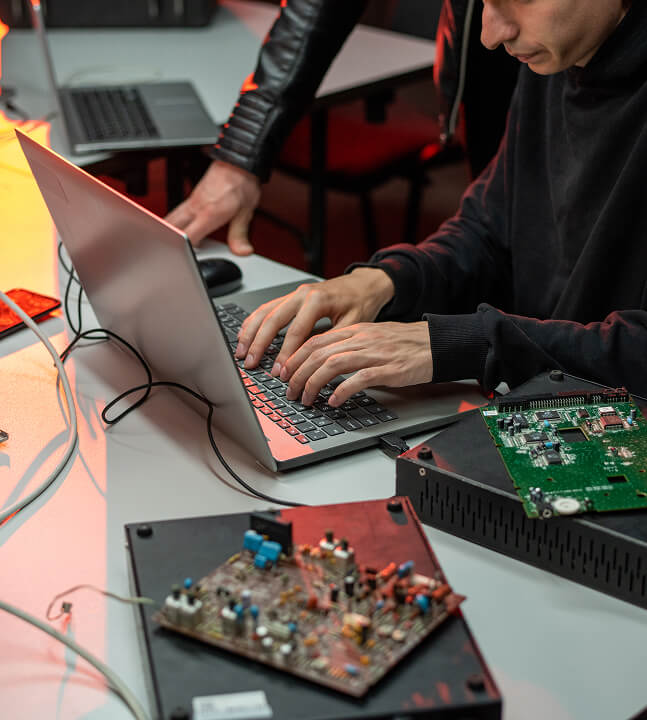 2 people working on one laptop with electronic devices around them