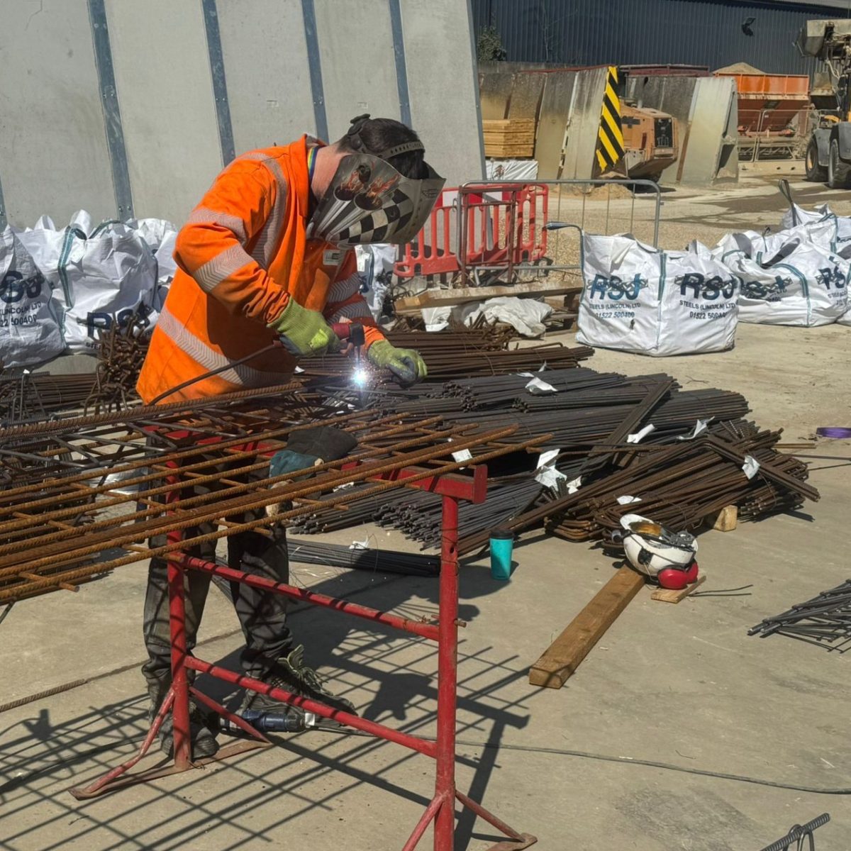 Land Based Engineering Technician Finn, welding outside in the yard, wearing a hi-vis jacket, protective gloves, and a welder's mask.