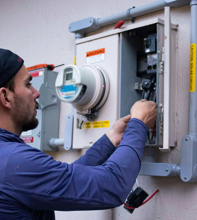 A man wearing blue, stood outside working with electrics.
