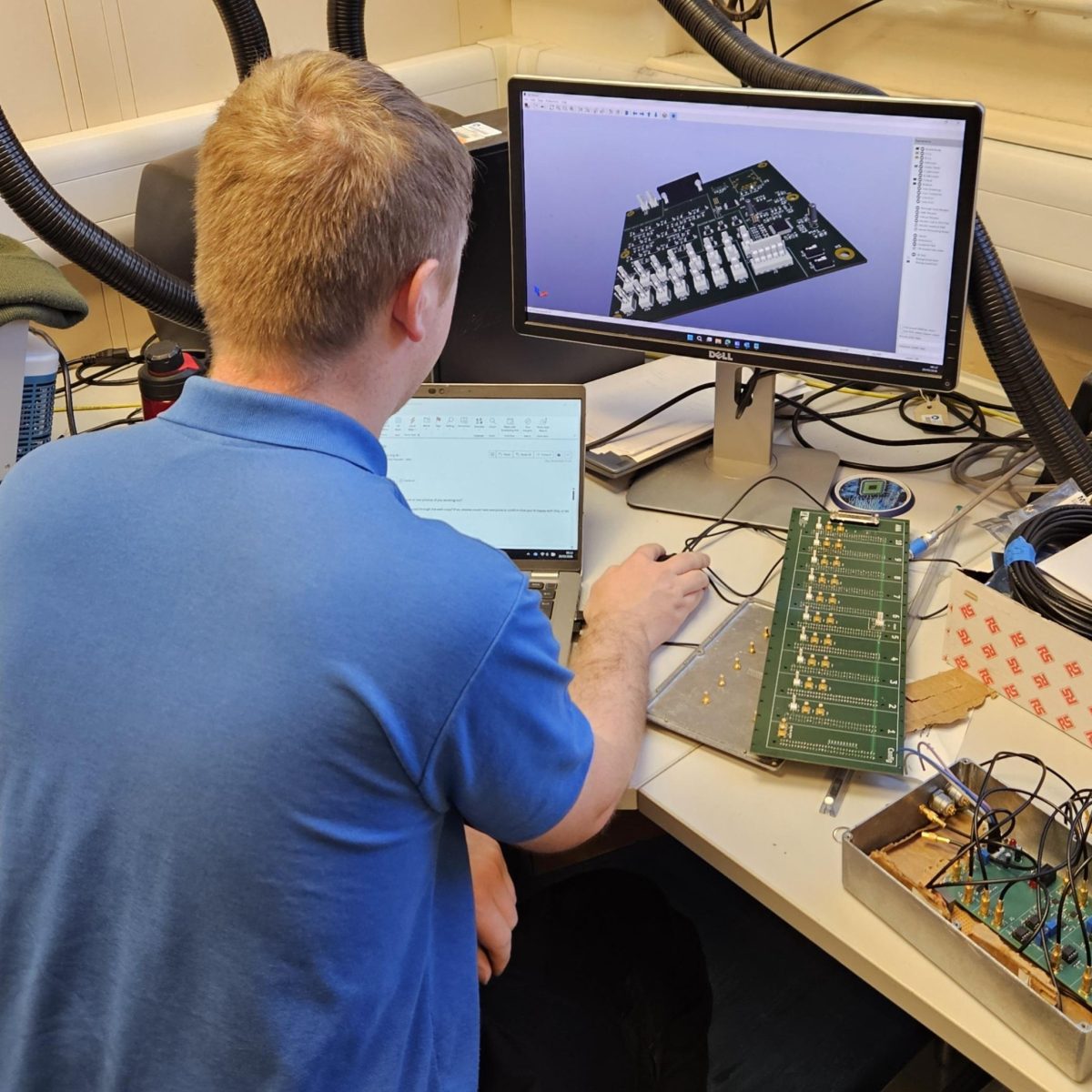 Electrical Engineering Technician Hayden sitting at a desk, using a laptop and monitor to design new circuitry.