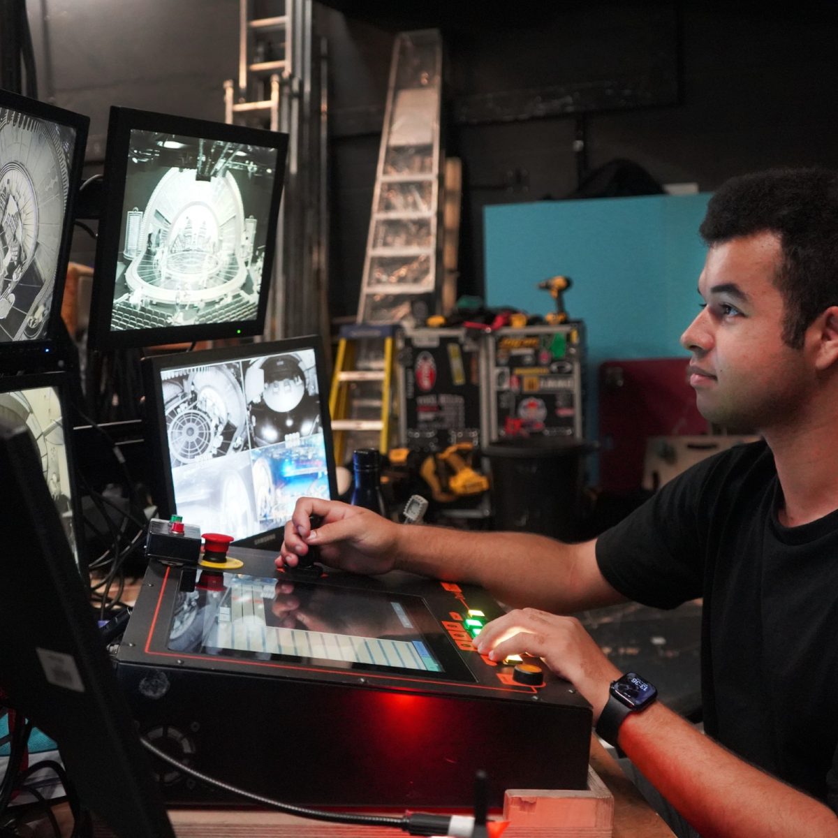 Creative Venue Technician Hugo, sitting at a lighting desk backstage, watching a show on monitors and controlling lighting cues.