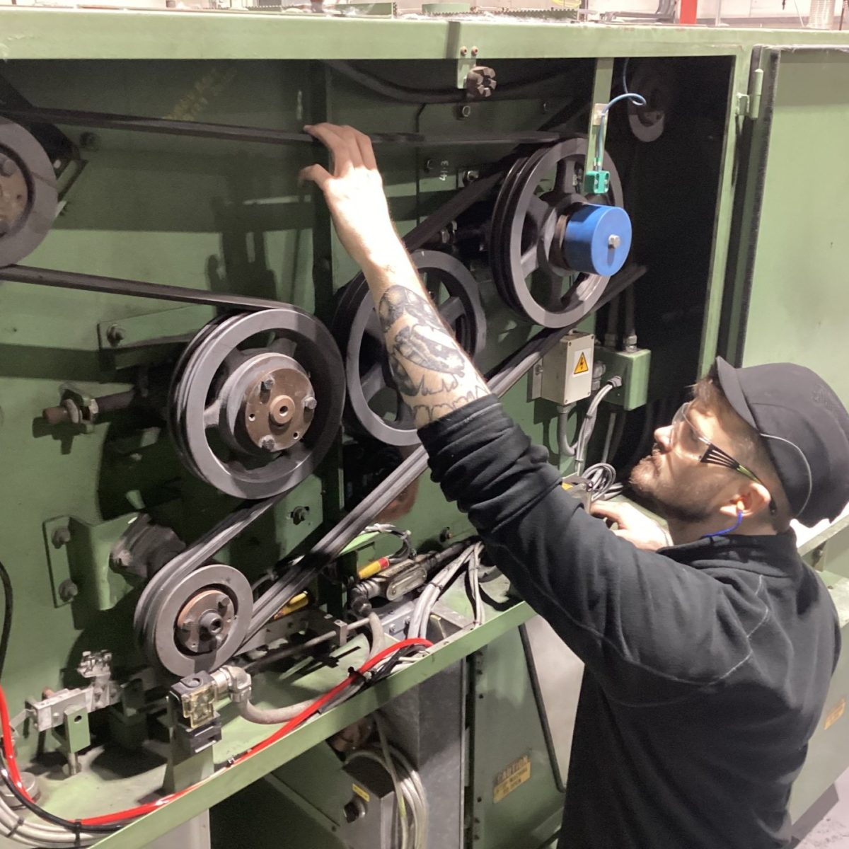 Maintenance and Operations Engineering Technician James, wearing safety glasses, fixing a machine containing a large belt drive.
