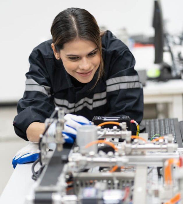 Woman in work jacket with high viz strips working on an electrical board.