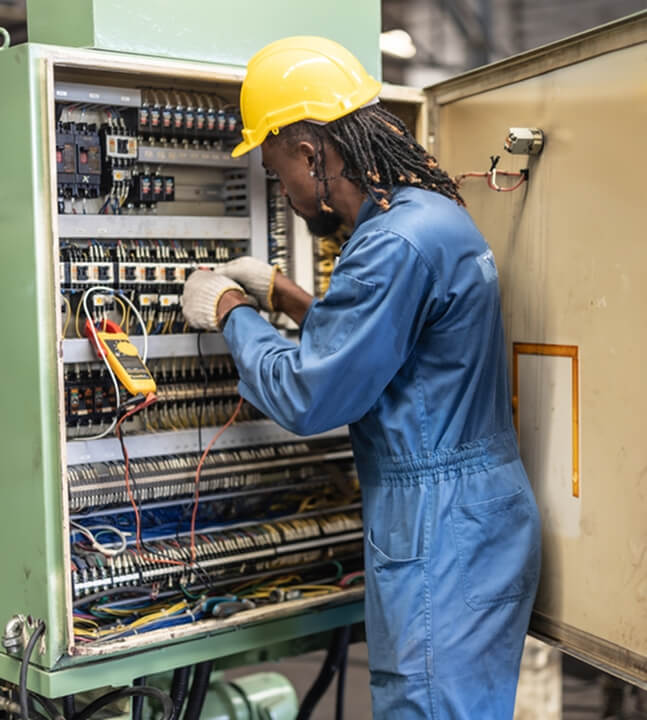 Man in blue overalls and yellow hard had working on an industrial size electric board.