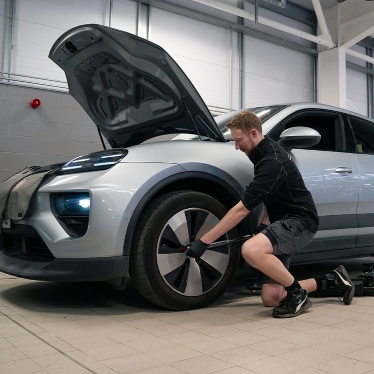 Electric Vehicle Technician Pete, kneeling down, working on the wheel of a car in the garage.