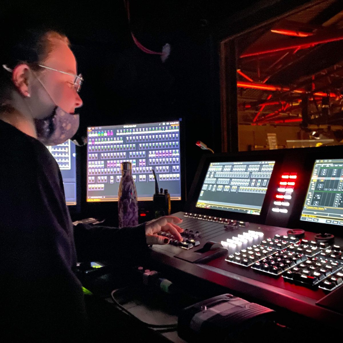 Creative Venue Technician Zoë, sat at a lighting and sound control desk, following the cues during a theatre show.
