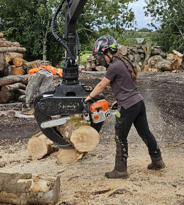 Tree and Forestry technician Matilda, wearing a helmet and face guard using a chainsaw to cut a log.