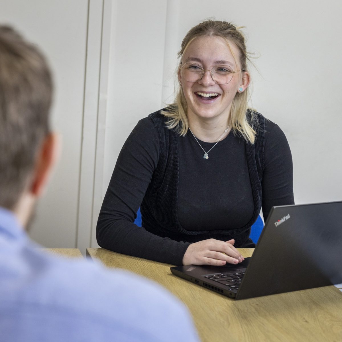 Data Technician Letty sat at a table with a laptop, chatting and laughing with someone sat across from her.