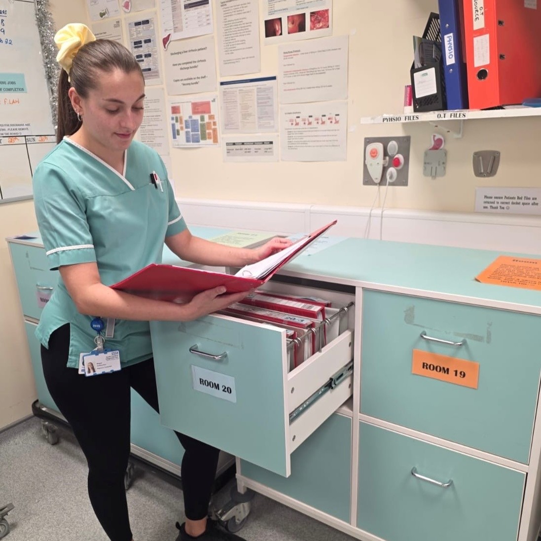 Pharmacy Technician Megan, wearing a healthcare tunic, looking in a ring binder of medical records,