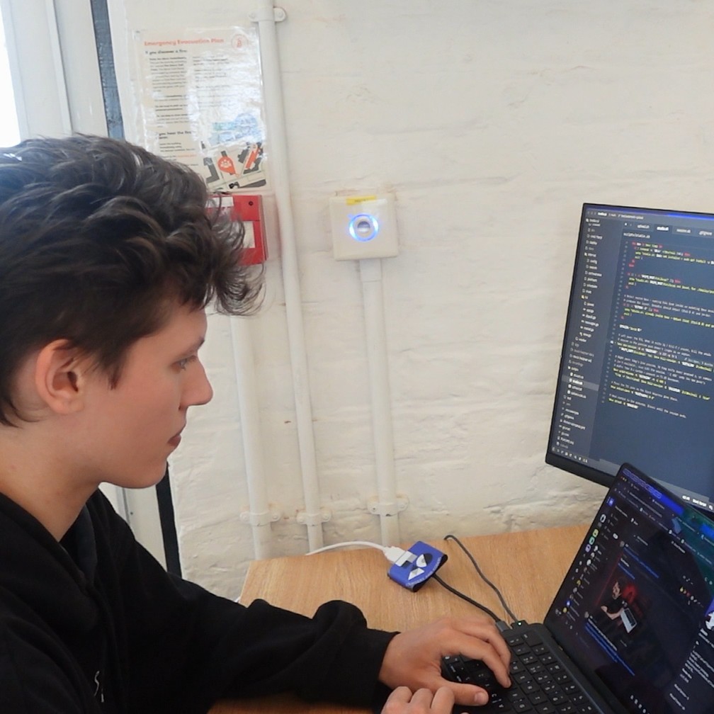 Software Developer Jaz, working on their laptop, at a desk, with code on the screen.