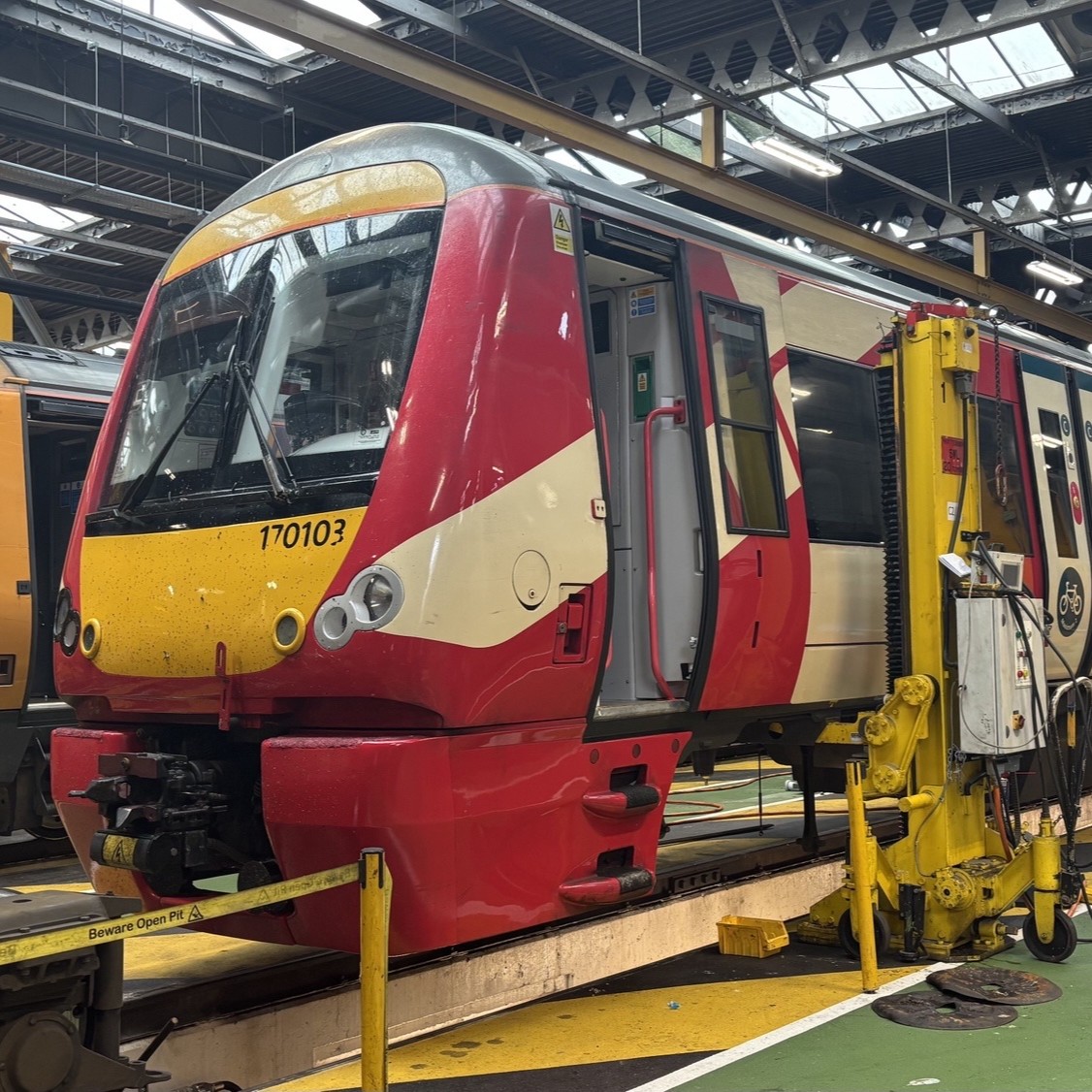 A red and yellow train, beside maintenance equipment, in a rail depot workshop.
