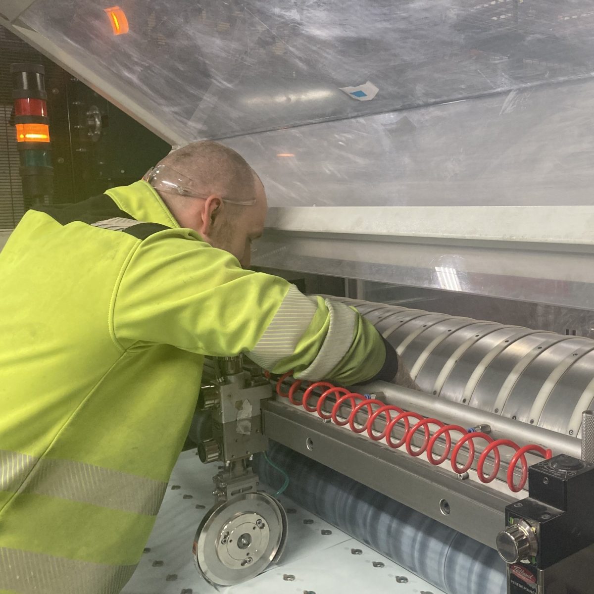 Print Technician Michael, wearing a hi-vis jacket, reaching into an industrial machine, in a manufacturing workshop.
