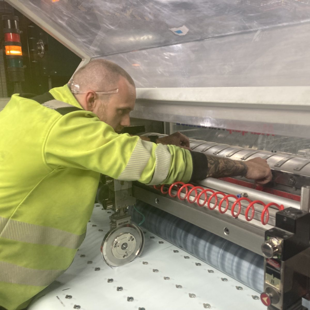 Print Technician Michael, wearing a hi-vis jacket, reaching into an industrial machine, in a manufacturing workshop.