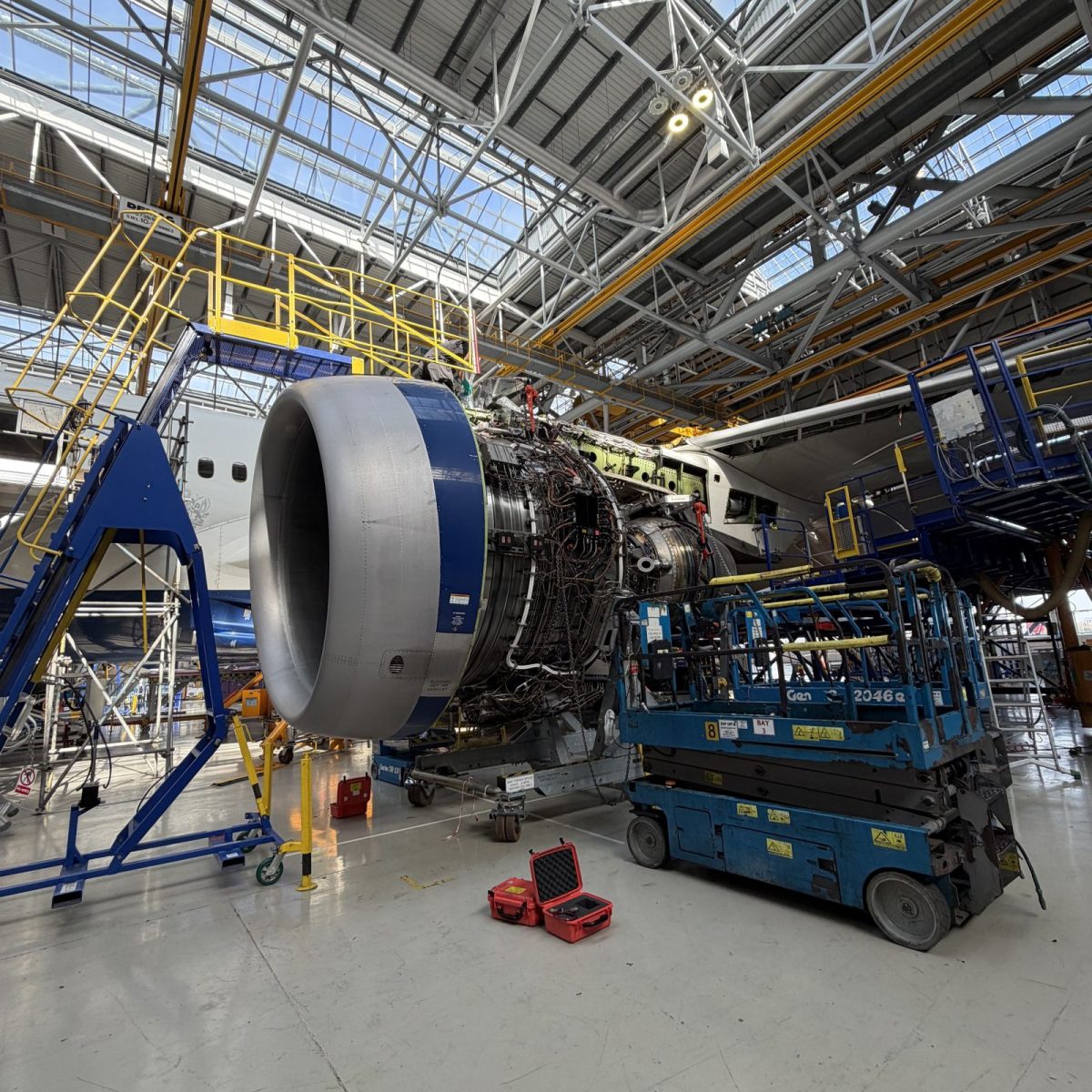 An aircraft in a hangar, with the inner workings of its jet engine exposed, with tools and equipment all around.