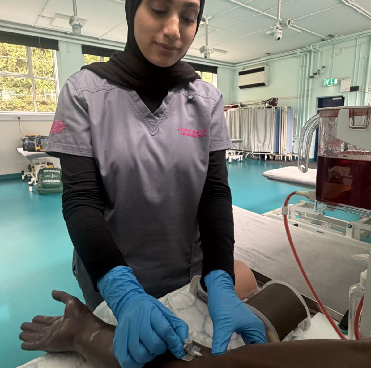 Simulation Technician Aliya, in a simulated ward, inserting a cannula into the arm of a simulation mannikin.